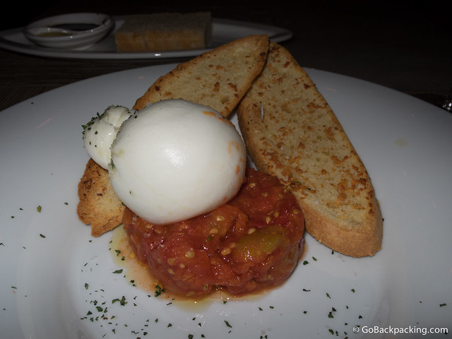 The Burrata is composed of fresh mozzarella presented on a bed of tomatoes, with crusty bread and a touch of sea salt 